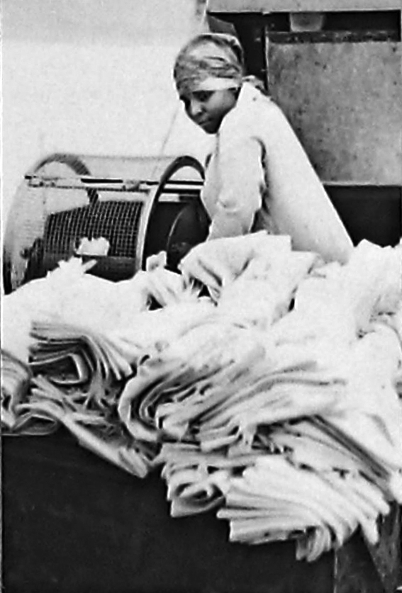 ‘Women and Work’ 1975 ©Hackney Flashers Image from ‘Women and Work’ 1975 shows a woman working a laundry, moving large amounts of cloth out of a machine.