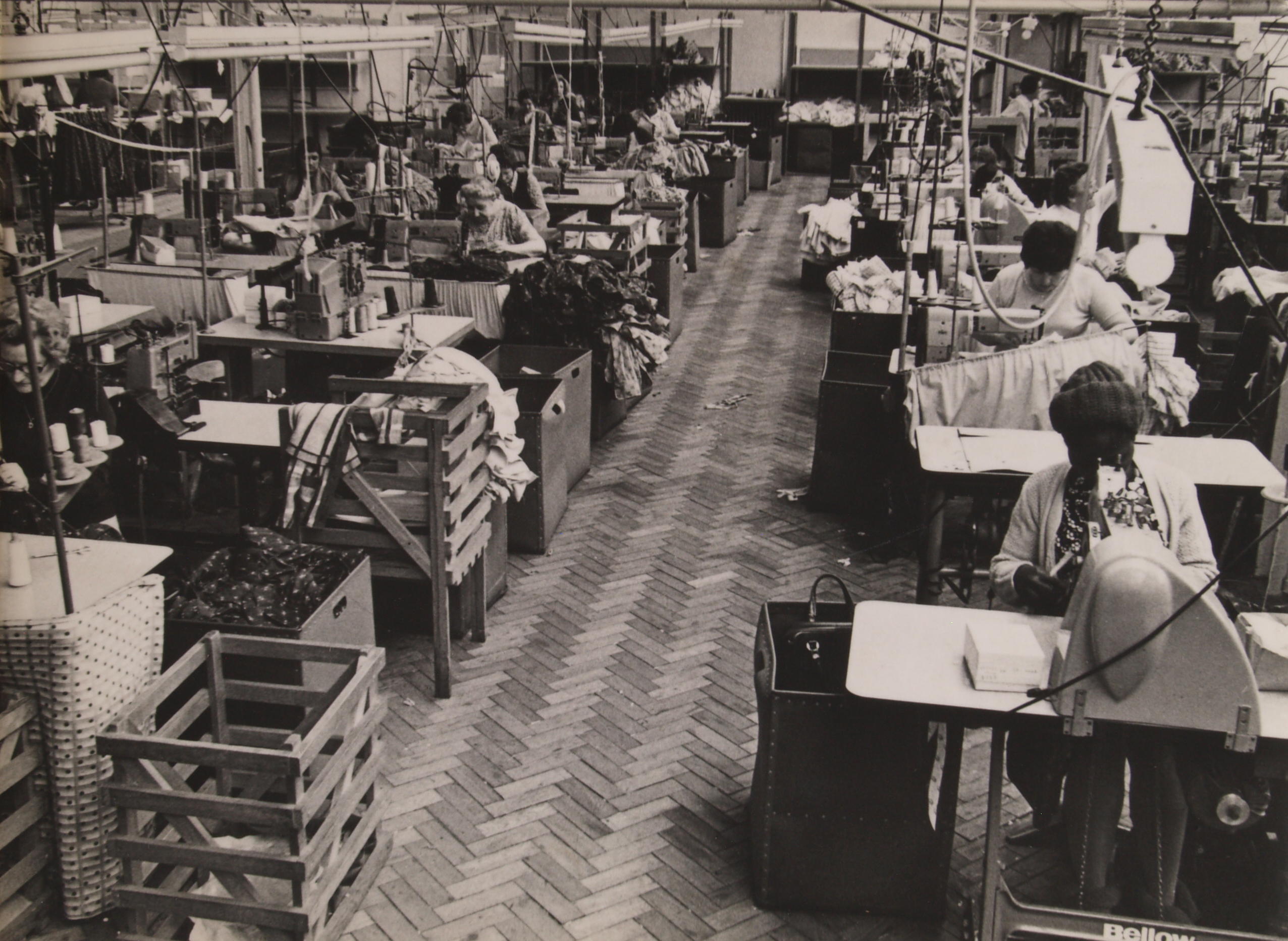 ‘Women and Work’ 1975 ©Hackney Flashers Image from ‘Women and Work’ 1975 shows rows of benches in a factory where women work on garment production.
